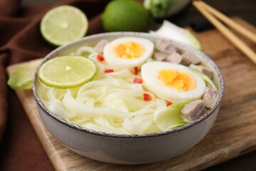 Bowl of delicious rice noodle soup with meat and egg on wooden board, closeup