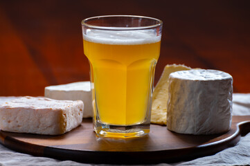 Glass of Belgian white unfiltered beer with notes of coriander and orange peer and wooden board with variety of belgian cheeses