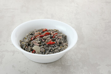 Nasi Goreng Cumi Hitam or Black Squid Fried Rice, served in white plate on wooden table
