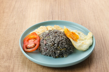 Nasi Goreng Cumi Hitam or Black Squid Fried Rice, served in white plate on wooden table
