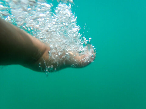 Swimmer swims in the sea, young man in wetsuit underwater with bubbles all around him in Mediterranean sea, A man's hand swimming underwater with bubbles around it, Professional male swimmer swim.