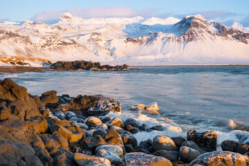 Sunrise over stunning winter landscape in Iceland. Snowy ocean coast with volcanic mountains and yellow grass. Pure nature at winter season.