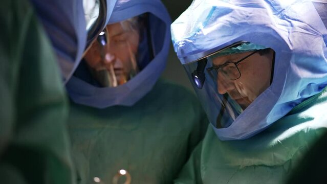 Group of surgeon in protective suits cooperate at surgery. Three professionals focused on operation.