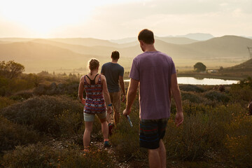 Friends hiking, walking in countryside at sunset with fitness and bonding in nature with travel and freedom. Exercise, adventure with men and woman walk through meadow or field with back view