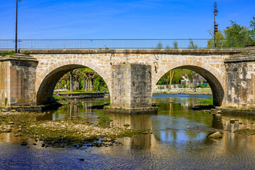 Fototapeta na wymiar Arches of the stone bridge spanning the river Loing in the medieval town of Moret-sur-Loing in Seine et Marne, France