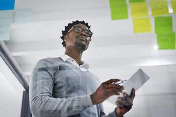 Business tablet, glass wall and black man brainstorming, strategy or research ideas in office. Sticky notes, planning and African male professional with technology for working, schedule and low angle