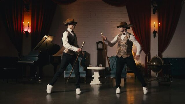 Music video, night show or event 4K. Two guys in dandy style outfit synchronically dancing in retro theatre stage. Classy male dancers performing in jazz funk style, dancing with classic cane in hands