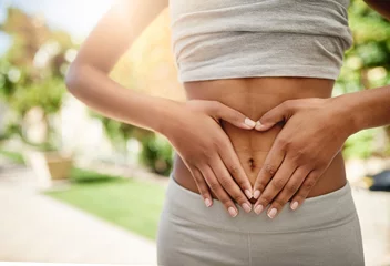 Tuinposter Hands, woman in park and stomach fitness, diet and nature for gut health, lipo and wellness for body workout. Gym, healthcare and tummy tuck, girl with heart hand sign on abdomen for exercise goals. © Donson/peopleimages.com