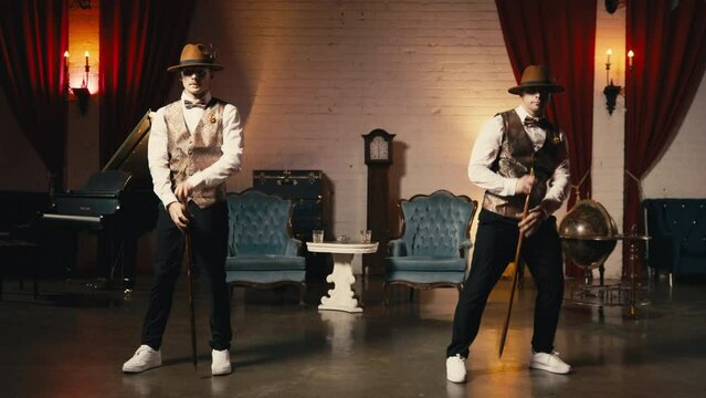 Cinematic RED camera shot of two stylish professional male dancers in dandy hat throwing each other classic cane stick, turning around and stop looking at camera in synchron. Funk dance move element