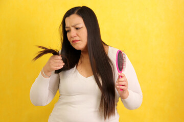 Adult Latina woman with very long hair worries and suffers while brushing because her hair falls...