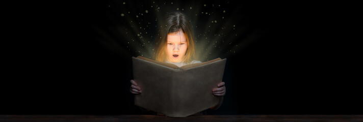 Surprised little girl reading magic book at night on dark background. Empty space for text