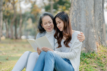 Grown daughter with aging mother expressing love and looking at memory notebook under tree in public park