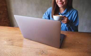 Closeup image of a young woman drinking coffee while working on laptop computer