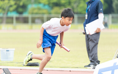 陸上大会でリレーを走る小学生の男の子