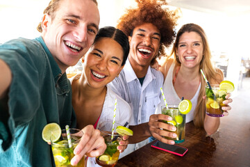 Multiracial friends taking selfie at beach bar looking at camera having cocktails. Friends having...
