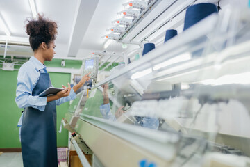 Obraz premium american female designer A sewing machine control panel is being used to design clothing in a large weaving industry. In her hand she has a tablet to see customer orders that have been made.
