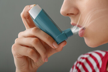Young woman using inhaler on grey background, closeup