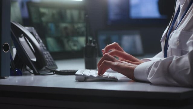 Female security officer works in police monitoring center. Woman types on keyboard, uses landline phone and radio set. Surveillance cameras view displayed on computer and tablet screens. Close up.