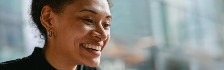 Smiling woman recording audio message on mobile phone while while sitting in cozy cafe near window
