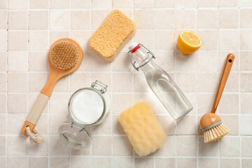 Bottle of vinegar, baking soda, brushes and sponges on light tile background
