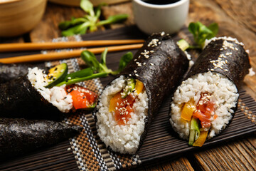 Bamboo mat with tasty sushi rolls on wooden background, closeup
