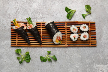 Bamboo mat with tasty sushi cones, rolls and lambs lettuce on grunge background