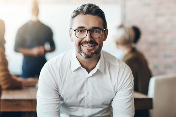 Leadership, portrait of ceo or businessman smile and sitting in office at work with colleagues behind manager. Entrepreneur or business, leader and smiling male person with glasses sit at workplace