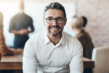 Obraz premium Leadership, portrait of ceo or businessman smile and sitting in office at work with colleagues behind manager. Entrepreneur or business, leader and smiling male person with glasses sit at workplace