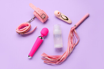 Bottle of lubricant with vibrators, handcuffs and whip on lilac background