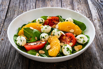 Mozzarella salad with leafy greens, orange and tomatoes  on wooden table
