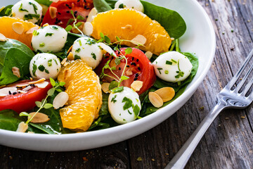 Mozzarella salad with leafy greens, orange and tomatoes  on wooden table
