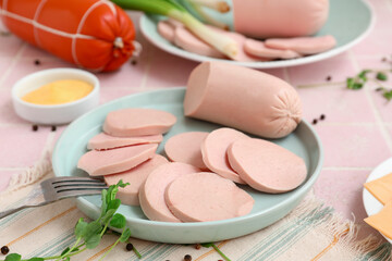 Composition with boiled sausage in plate, green onion and sauce on pink tile table