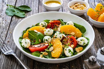 Mozzarella salad with leafy greens, orange and tomatoes  on wooden table
