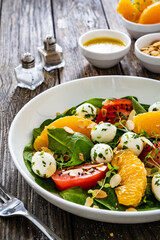 Mozzarella salad with leafy greens, orange and tomatoes  on wooden table

