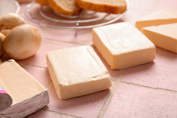 Processed cheese, bread and vegetables on pink tile background