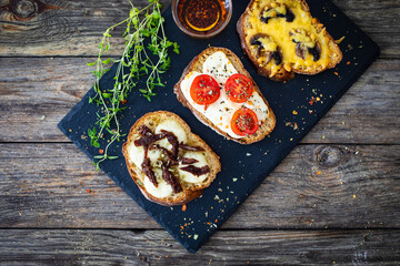 Tasty sandwiches - baked bread with cheese, olives, sun dried tomatoes, mushrooms and thyme on wooden table
