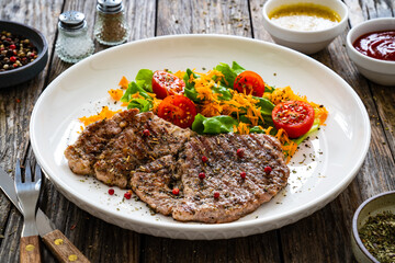 Grilled pork steaks with fresh vegetable salad on wooden table 