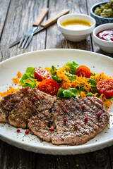 Grilled pork steaks with fresh vegetable salad on wooden table 