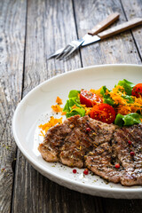 Grilled pork steaks with fresh vegetable salad on wooden table 