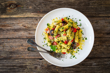 Rigatoni with sliced sausages, parmesan cheese and white mushrooms served on wooden table
