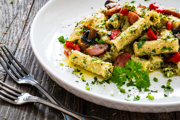 Rigatoni with sliced sausages, parmesan cheese and white mushrooms served on wooden table

