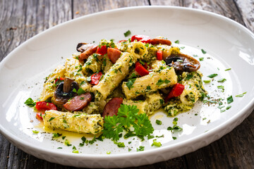 Rigatoni with sliced sausages, parmesan cheese and white mushrooms served on wooden table
