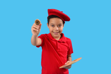 Little African-American artist with brush and paint palette on blue background. Children's Day celebration