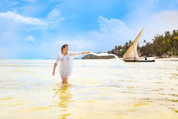 Beach holiday - beautiful woman holding shawl walking on sunny, tropical beach
