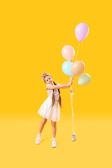 Little girl in crown with balloons on yellow background. Children's Day celebration