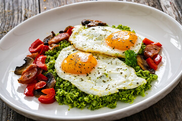 Breakfast - sunny side up eggs, grated broccoli, stir fried vegetables and sliced sausages served on wooden table
