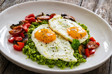 Breakfast - sunny side up eggs, grated broccoli, stir fried vegetables and sliced sausages served on wooden table
