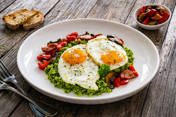 Breakfast - sunny side up eggs, grated broccoli, stir fried vegetables and sliced sausages served on wooden table

