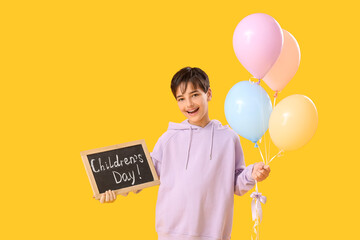 Little boy holding chalkboard with text CHILDREN'S DAY and balloons on yellow background