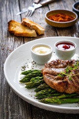 Barbecued pork neck and asparagus on wooden table